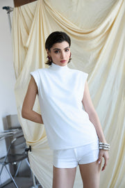 Woman wearing a white sleeveless top and shorts in front of beige curtains